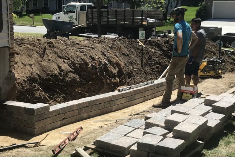 Workers building retaining wall with bricks and tools.